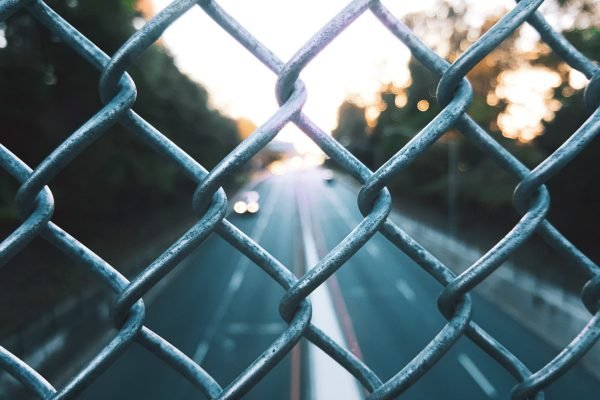 A selective closeup shot of chain link fence on the blurry background of a road
