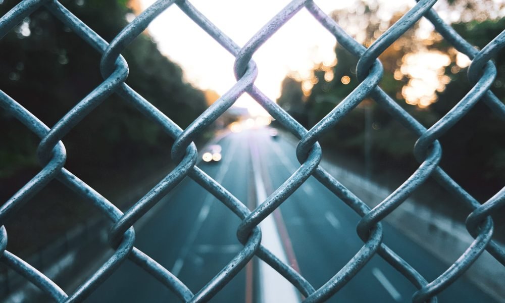 A selective closeup shot of chain link fence on the blurry background of a road